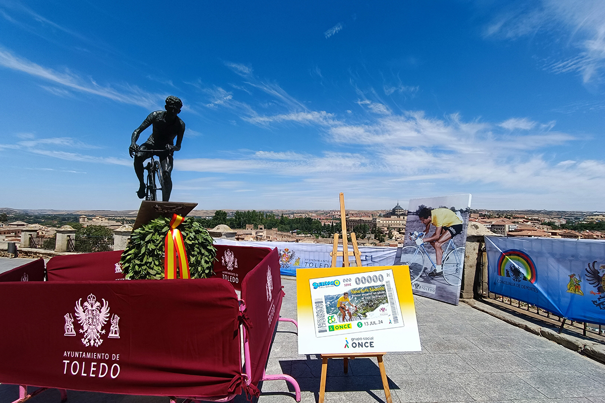 Estatua de Federico Martín Bahamontes en la zona de miradores junto al cupón que se le dedicó y con una imagen panorámica de Toledo de fondo