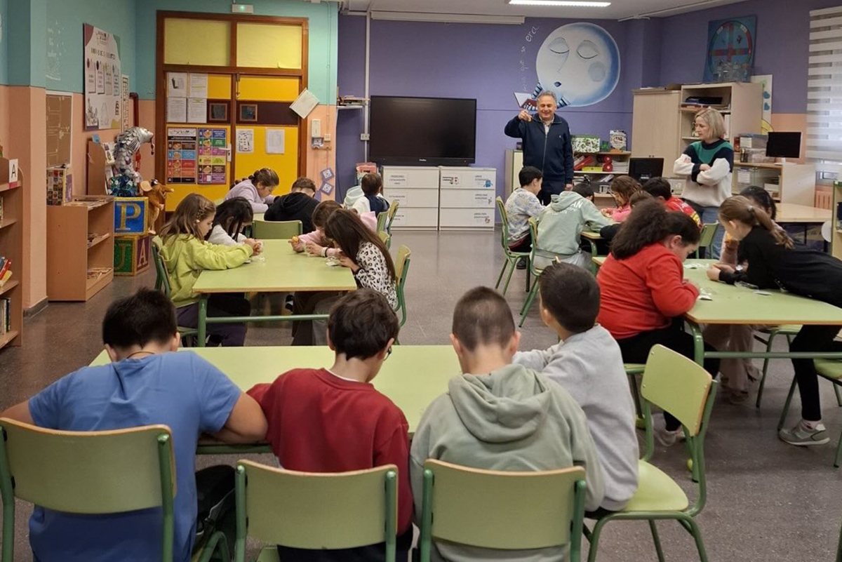 Carlos Javier en un aula hablando acerca del braille mientras los alumnos juegan con un llavero del signo generador