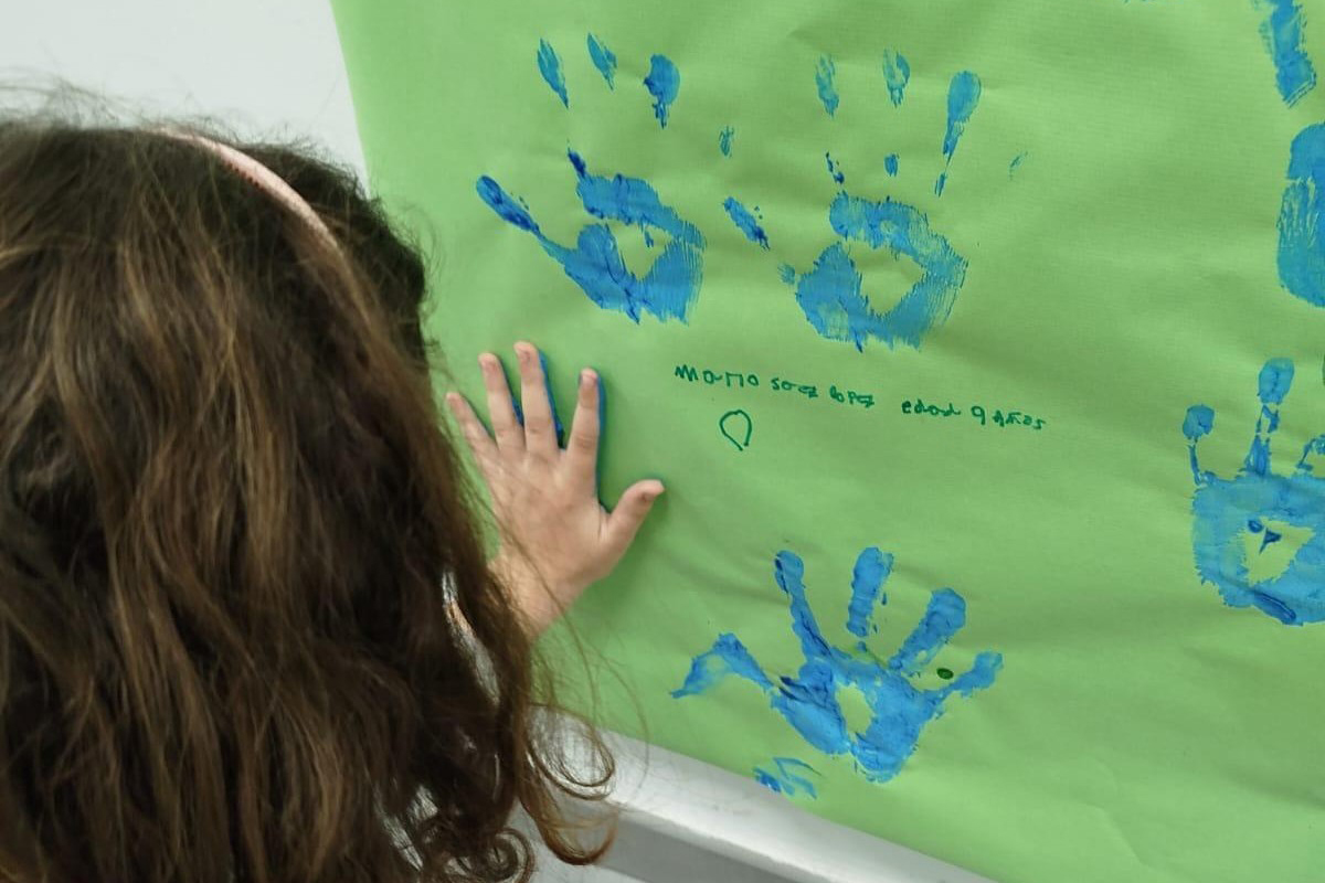 Una niña de espaldas dejando la huella de su mano con pintura en un mural