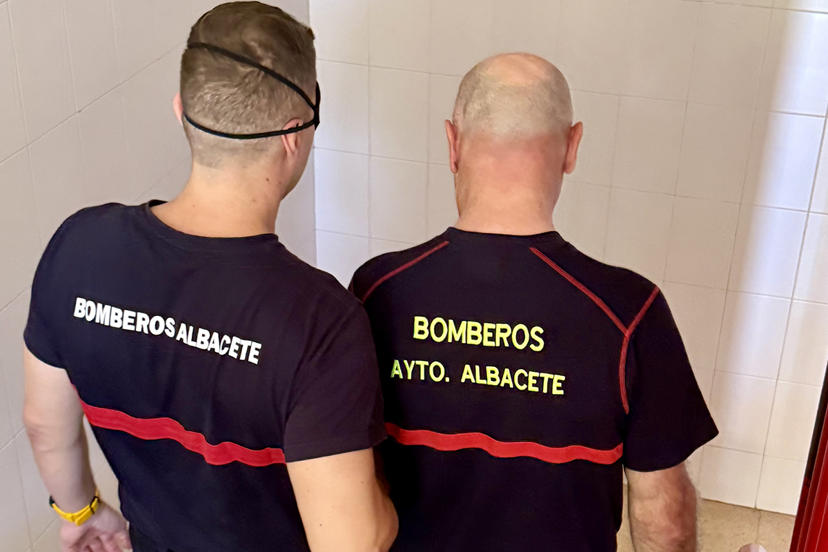 Dos bomberos de Albacete bajando unas escaleras, uno de ellos lleva el antifaz y se coge del brazo del otro, que le va guiando