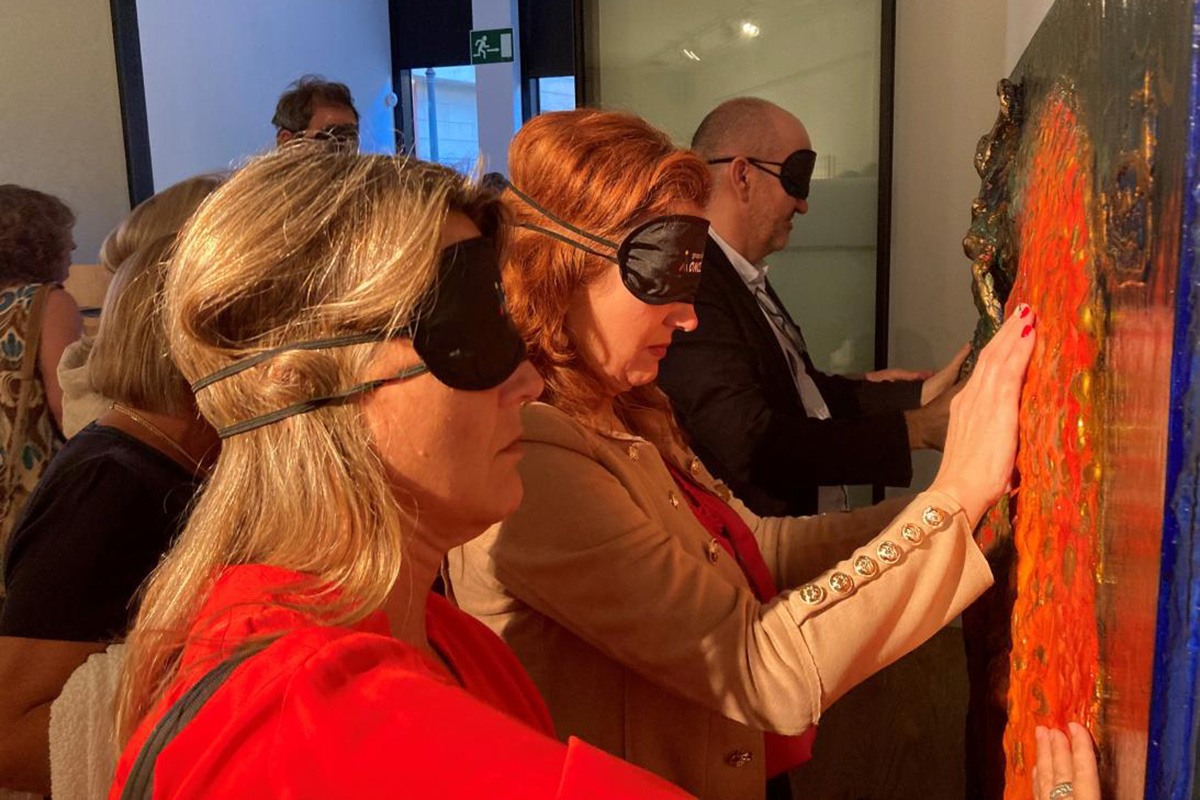 Personas con antifaz tocando los cuadros de la exposión 