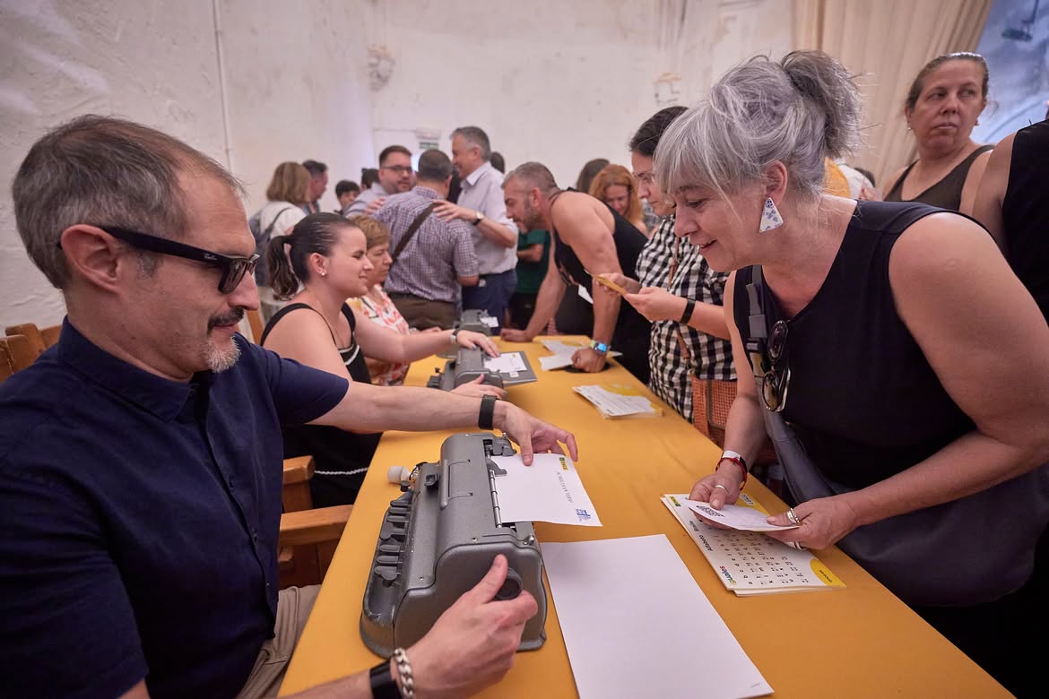Asistentes a Acaricia un verso pidiendo su nombre en braille mientras que personas ciegas se lo escriben con la máquina perkins