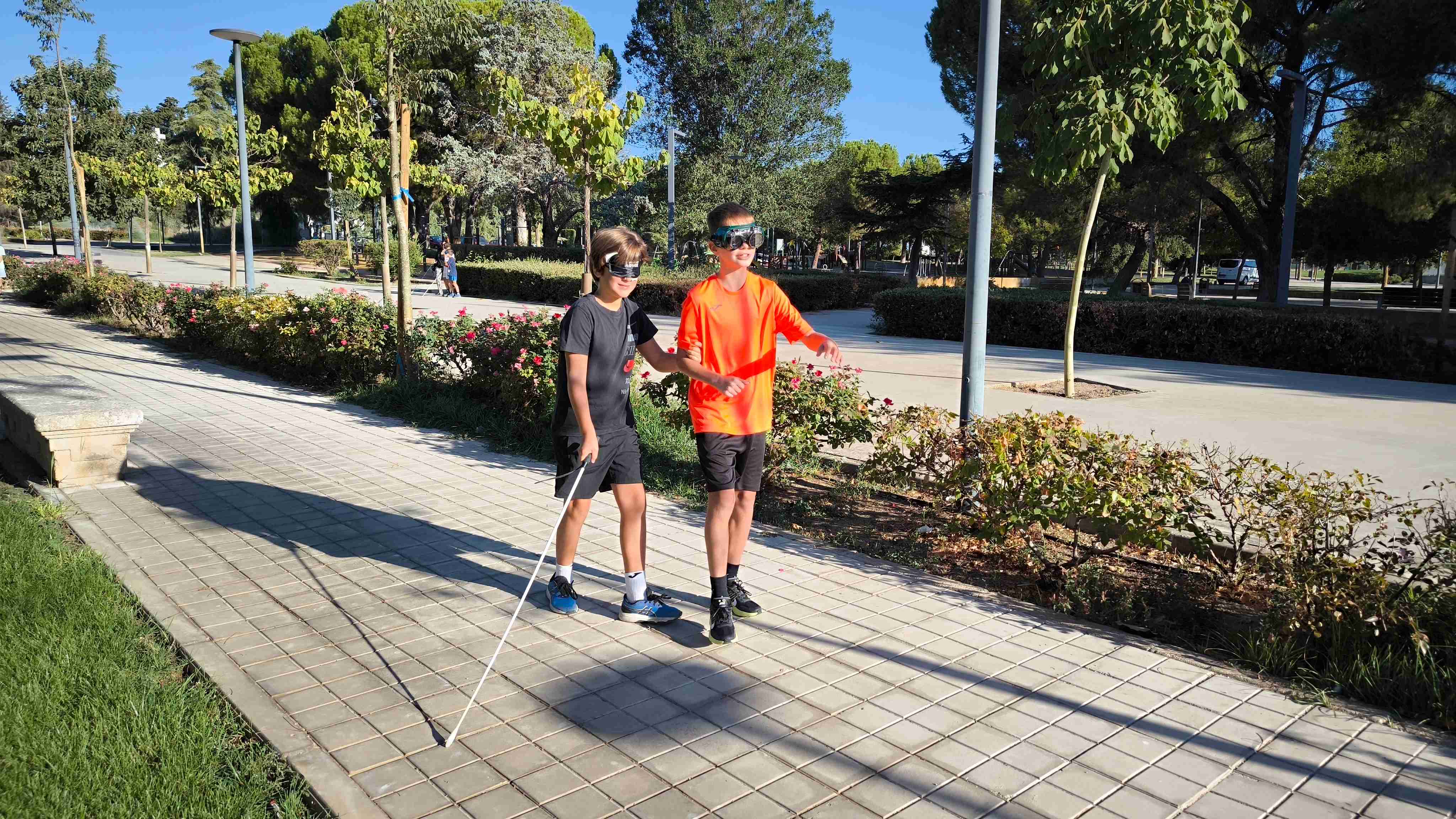 Dos alumnos realizando el recorrido. Uno lleva un antifaz y el bastón y el otro, que es quien ofrece su brazo para guiar, lleva unas gafas de simuación